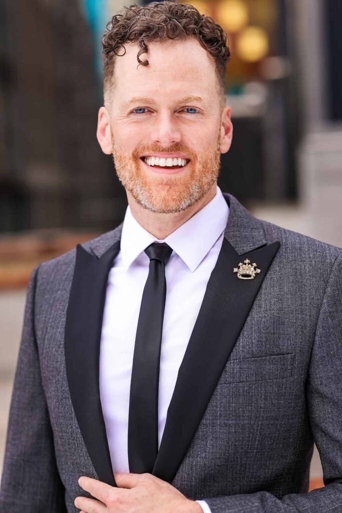 a smiling man in a suit and tie whose name is Leigh Cambre